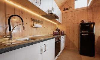 A modern kitchen with wooden panels and an elegant countertop. The space is well-lit and includes furnishings such as a refrigerator and kitchen appliances.