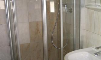A modern shower with glass doors and a simple faucet. The walls are brightly tiled and the atmosphere is friendly and clean.