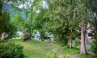 A quiet campsite surrounded by green trees. In the background, motorhomes and tents are visible.
