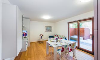 A bright, modern kitchen with a dining area. Large windows offer views of an outdoor space.