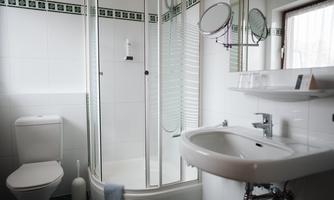 A modern bathroom with a shower, a sink, and a toilet. The walls are bright tiled and there is a window for natural light.