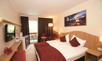A cozy hotel room with a double bed, a television, and a small table. The warm colors and inviting light create a relaxed atmosphere.