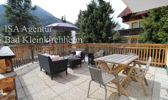 A cozy terrace with seating and a table. In the background, trees and mountains are visible.