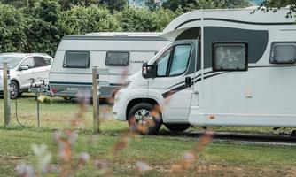 A campsite with caravans and a car. The surroundings are green and inviting.