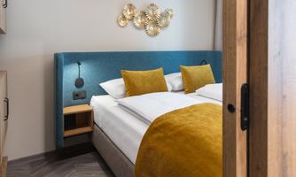 A modern bedroom with a blue headboard and comfortable yellow pillows. The room is bright and designed in a minimalist style.