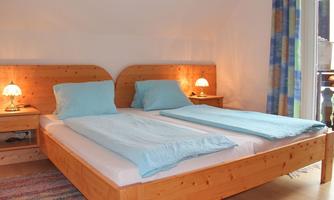 A bright bedroom with a large double bed and blue cushions. Two nightstands with lamps provide pleasant lighting.