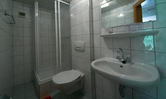 A small bathroom with a shower, a sink, and a toilet. The walls are tiled with white tiles.