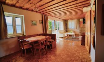 A cozy living area with wooden beam ceiling and a dining area. Large windows let in plenty of light and offer a view outside.