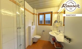 A modern bathroom with a shower, sink, and toilet. Large windows provide plenty of light.