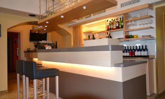 A modern bar with an elegant counter and chairs. In the background, there are shelves with wines and drinks visible.