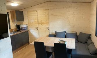A modern kitchen with a dining area in a wooden house. The decor is simple and cozy, with a table and comfortable seating.