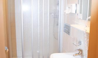A small bathroom with a separate shower and a sink. The floor is tiled and the walls are light-colored.