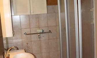 A small bathroom with a sink, a towel holder, and a shower cubicle. The walls are tiled and the ceiling has wood paneling.