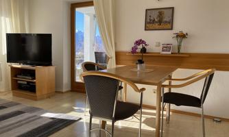 A cozy living area with a table and chairs. In the background, there is a TV and a window with a view of the mountains.