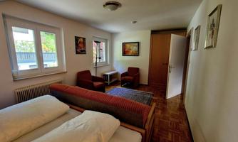A cozy room with two beds and red chairs. There is a window and decorative pictures on the walls.