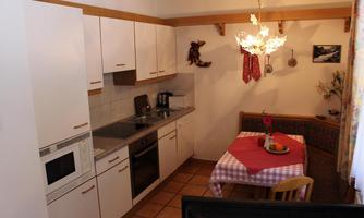 A bright kitchen with modern appliances and a dining area. The table is set with a red cloth and there is a cozy seating area.