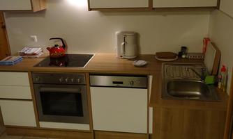 A modern kitchen with a wood countertop, stove, dishwasher, and sink. There is also a kettle and a red teapot on the countertop.