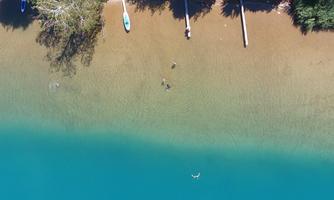A beautiful lake with clear, turquoise water. On the shore, some trees and boats can be seen.