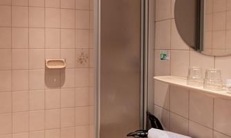 A modern bathroom with a shower and a sink. The walls are light tiled, and there are towels on the sink.