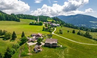 A picturesque landscape with a small village surrounded by green meadows and mountains. Clouds drift by in the blue sky.