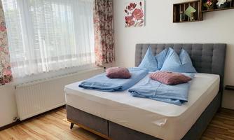 A bright bedroom with a cozy bed and colorful curtains. On the bed are cushions and blankets in soft colors.