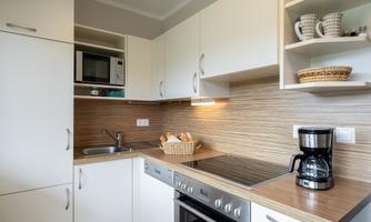 A modern kitchen with white cabinets and wooden surfaces. There is a stove, a microwave, and a coffee machine.
