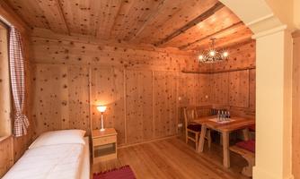 A cozy room with wooden walls and a warm ambiance. There is a bed, a table with chairs, and soft lighting.