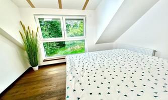 A bright bedroom with a bed and a pattern of greenish triangles. Large windows provide a view of the greenery.