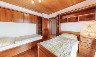 A simple bedroom with two beds and wooden shelves. The cozy atmosphere is enhanced by warm light and wooden paneling.
