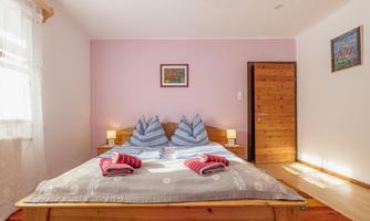 A cozy bedroom with a large bed and colorful pillows. The walls are painted in soft tones, and there is plenty of natural light.