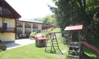 A playground with a slide and a swing in a green garden. In the background, you can see a cozy building with balconies.