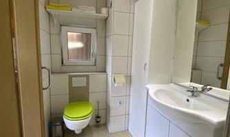 A modern bathroom with bright tiles, a sink, and a toilet. The window provides daylight and fresh air.