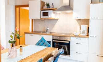 A modern kitchen with bright cabinets and wooden countertops. A table with a vase and chairs creates an inviting atmosphere.