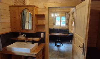 A cozy bathroom with wooden shelves and a modern sink. Through the open door, you can see an inviting living area with a round table and a seating area.
