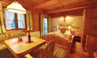 A cozy room with wooden walls, a large bed, and a dining area. The warm colors and the windows let in plenty of light.