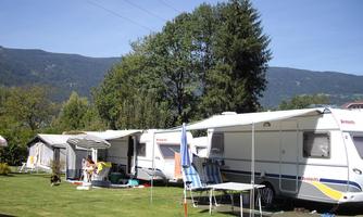 A campsite with caravans in a green meadow. In the background, mountains and trees can be seen.