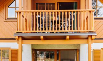 A cozy house with orange wood design and a balcony. In front of the front door, there is a table with chairs in a beautiful garden.