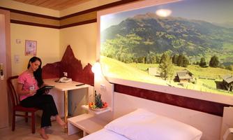 A cozy room with a bed and a table. On the wall, there is a large picture of a beautiful mountain landscape.