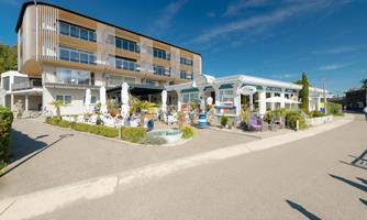 A modern building with a terrace and several sun umbrellas. The outdoor area is invitingly designed and surrounded by plants.
