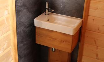 A modern wash basin in a corner of a wooden room. The walls are made of wood and stone, creating a cozy atmosphere.