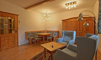 A cozy living room with wooden shelves and a dining table. There are two comfortable armchairs and a table in the middle of the room.