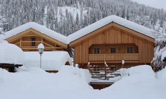 Two charming wooden houses in the snow, surrounded by a picturesque winter landscape. The roofs are covered with a thick layer of snow.