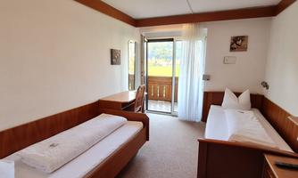 A bright room with two single beds and a table. There is a balcony with a view and large windows for plenty of daylight.