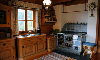 A cozy kitchen in rustic style with wooden cabinets and a traditional stove. The room has large windows that provide plenty of light and a view outside.