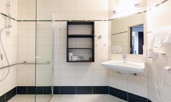 A modern bathroom with a walk-in shower and a sink. Bright tiles and a minimalist design create a clean atmosphere.