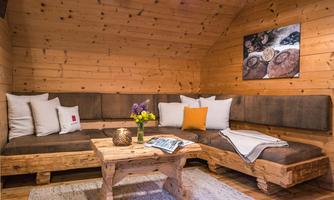 A cozy living area with wooden walls and a comfortable seating arrangement. A table with a flower vase and decorative elements creates an inviting atmosphere.