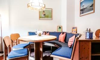 A cozy dining area with a round table and benches. The walls are decorated with pictures, and there is a warm atmosphere.