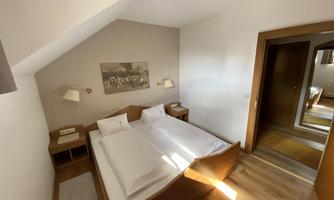 A cozy room with two single beds and a warm wooden floor. A piece of art hangs on the wall, and there are nightstands with lamps.