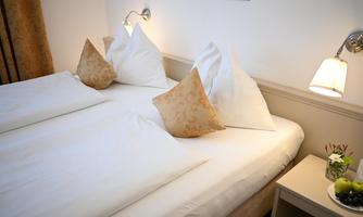 A cozy hotel room with two beds and decorative pillows. Next to the bed is a nightstand with fresh fruit and a small flower arrangement.
