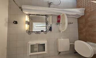 A small bathroom with a shower, a sink, and a toilet. The walls are tiled and there is a mirror above the sink.